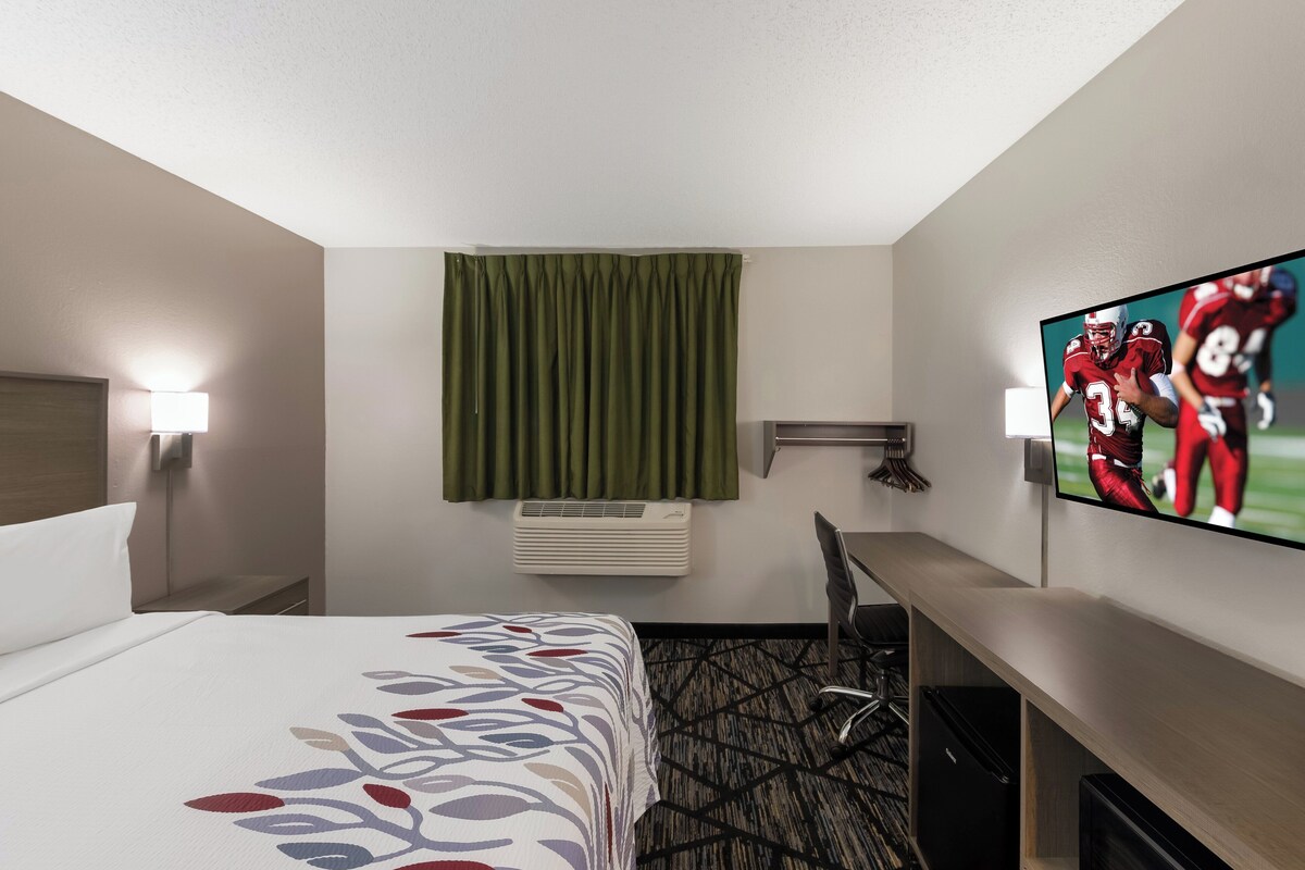 A hotel room with a bed, a desk, a television, and a window with curtains.