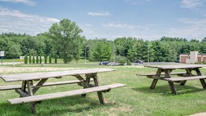 A picnic area with wooden tables and benches, surrounded by grass and trees.
