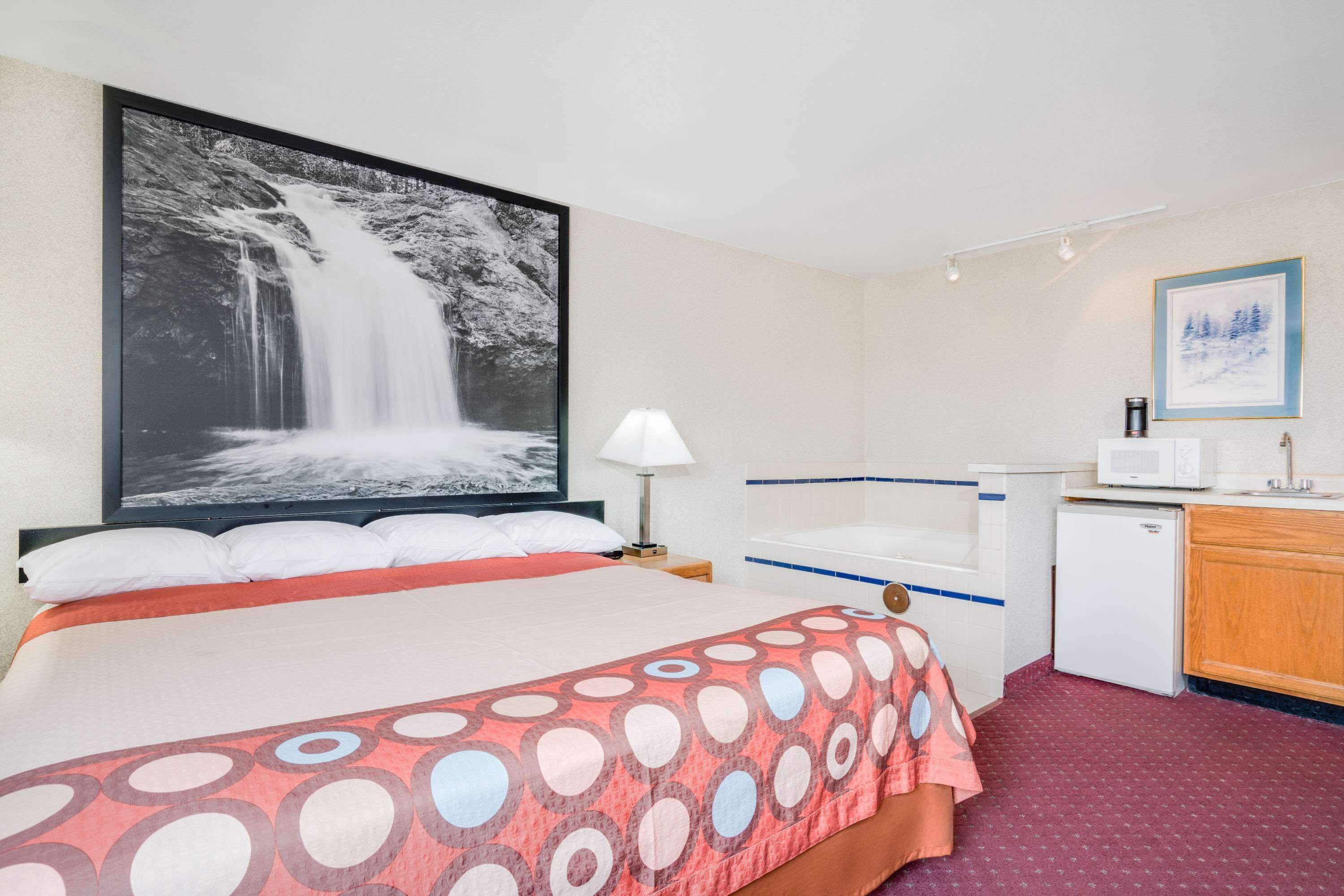 A hotel room with a large bed, a small kitchenette, a microwave, a refrigerator, and a bathroom with a shower and sink.