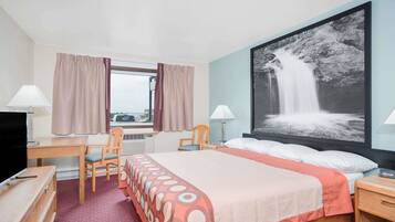 Habitación de hotel con cama, escritorio, silla, televisión y un cuadro grande de una cascada en la pared.
