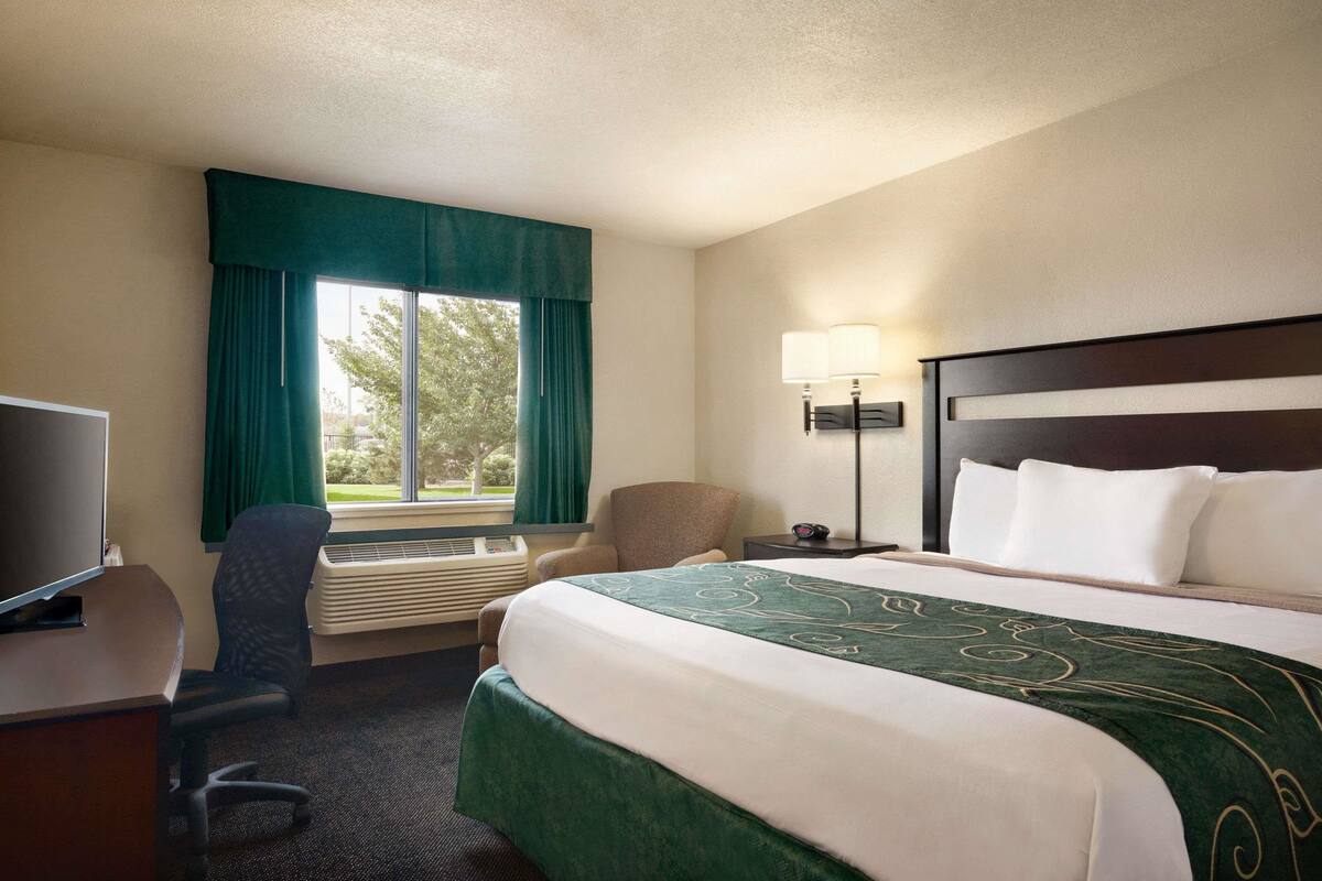 Una habitación de hotel con cama, escritorio, silla, televisión y ventana con cortinas.
