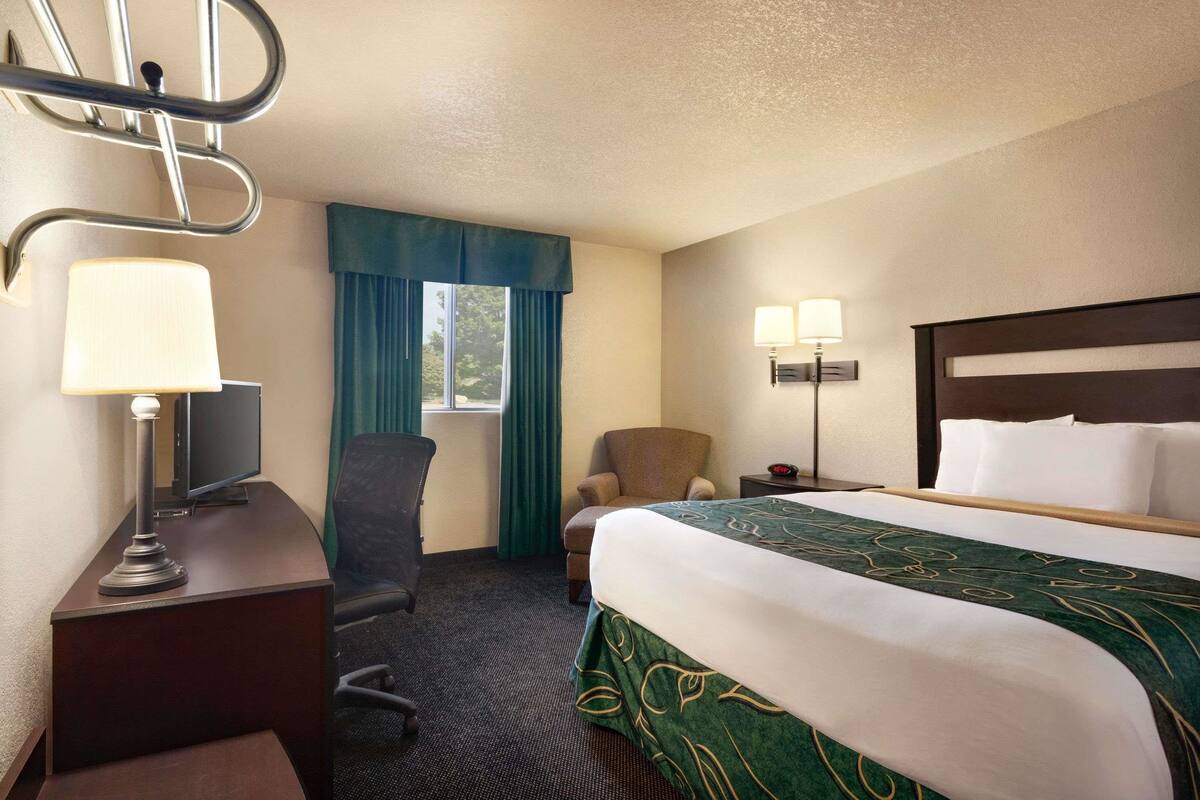 Habitación de hotel con cama, escritorio, silla, lámpara y ventana con cortinas.