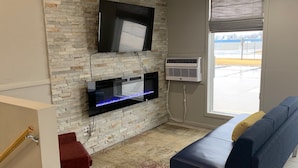 A modern living room with a stone wall, a flat-screen TV, a built-in fish tank, a blue sofa, and a large window with a view of a parking lot. - Super 8 by Wyndham Kirksville-University Area (Kirksville)