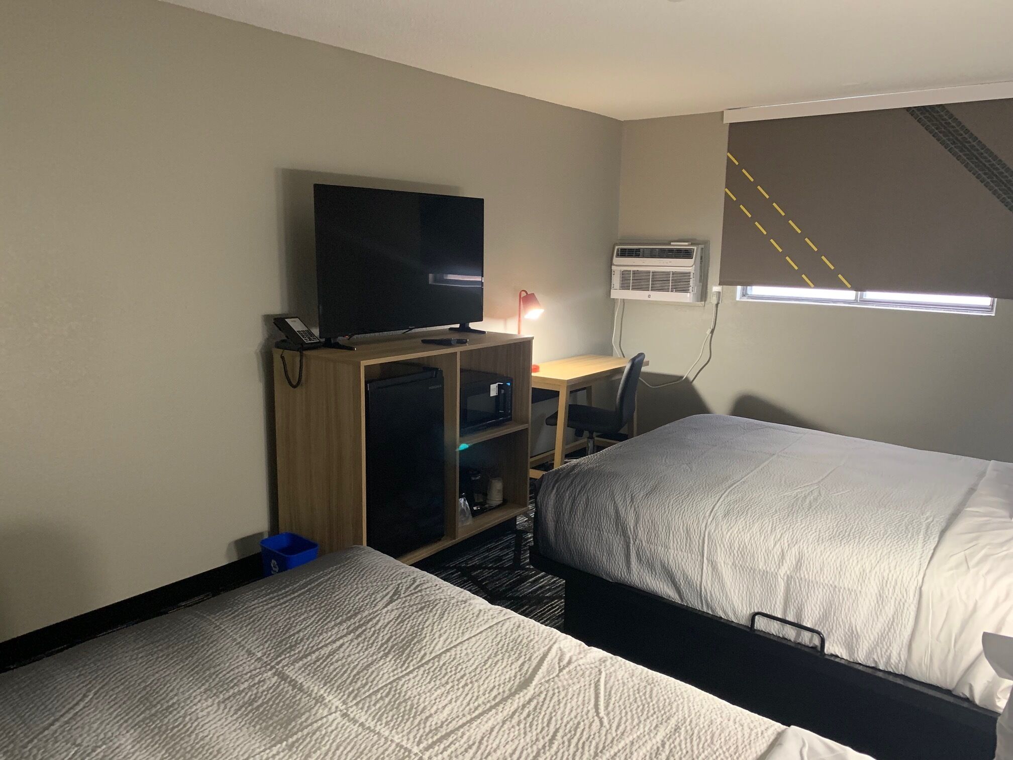 Une chambre d’hôtel avec deux lits, un bureau avec une chaise, une télévision et un appareil de climatisation.