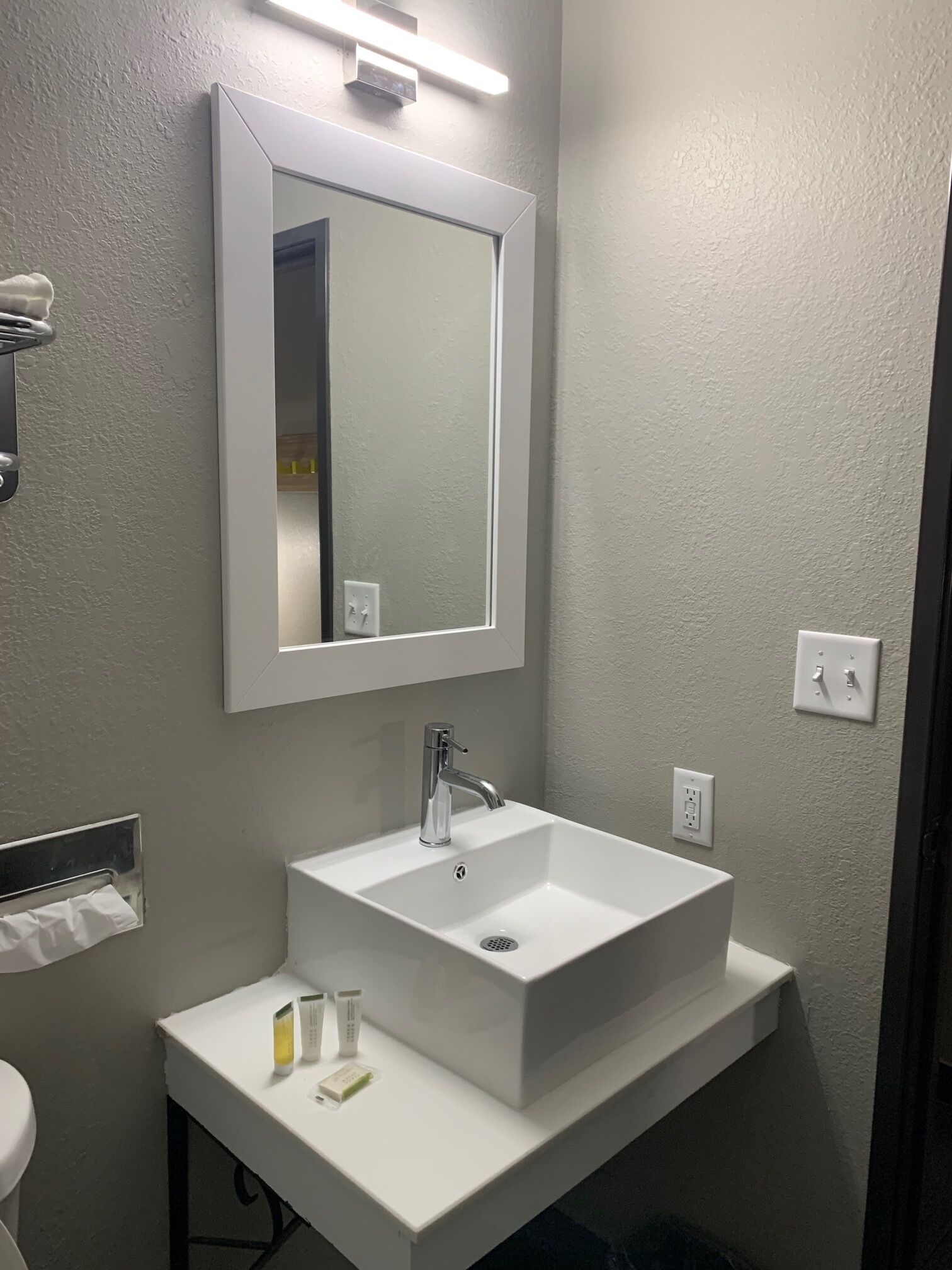 A bathroom with a white sink, a mirror, and a towel dispenser.