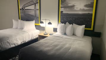 Una habitación de hotel con dos camas, una mesita de noche con lámpara y dos cuadros en la pared.