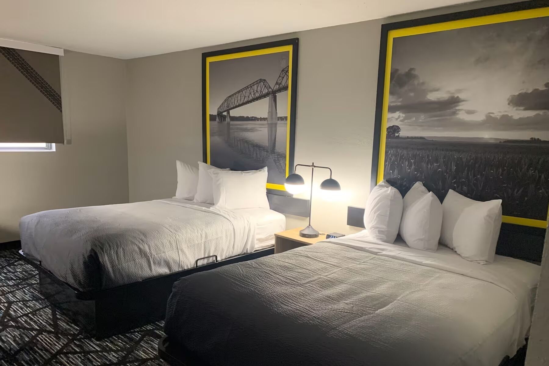 A hotel room with two beds, a nightstand with a lamp, and two large framed pictures on the wall.