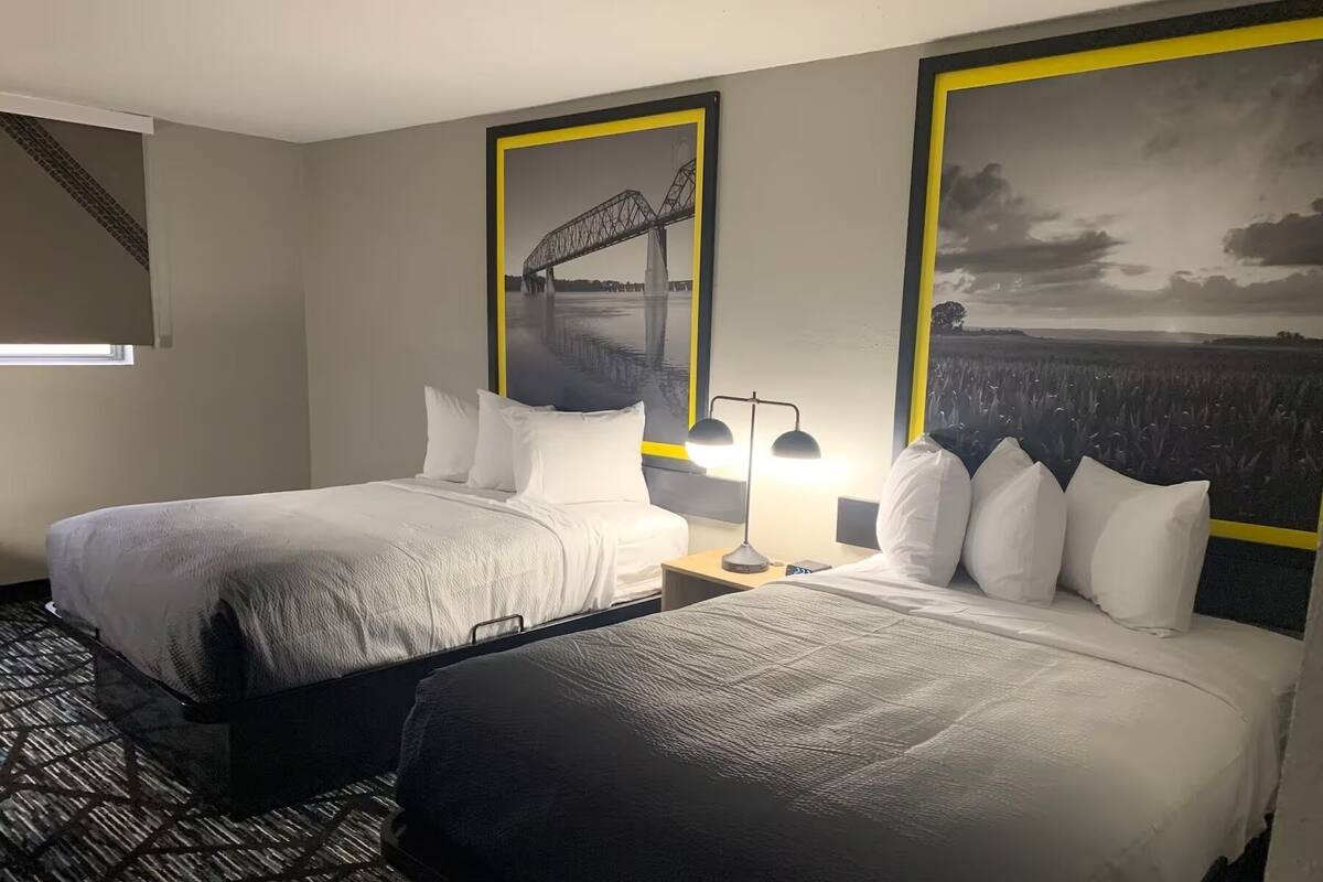 A hotel room with two beds, a nightstand with a lamp, and two large framed pictures on the wall.