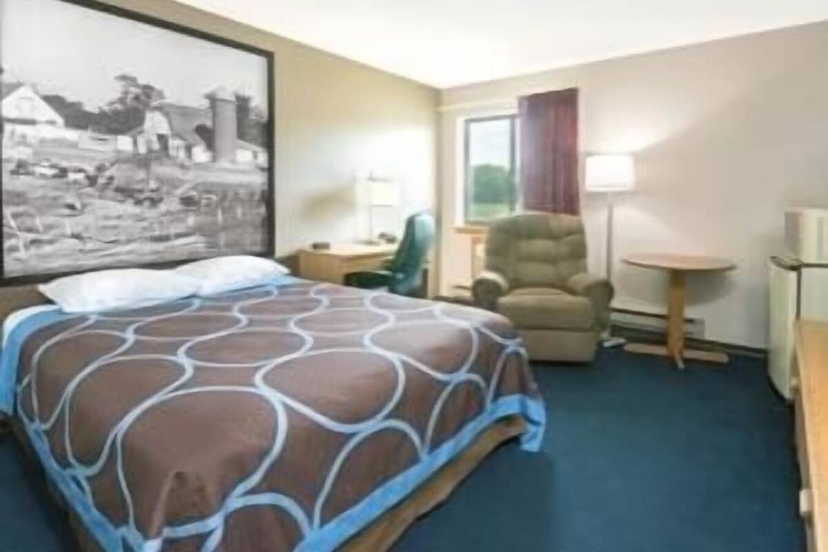 A hotel room with a bed, a chair, a small table, and a lamp.