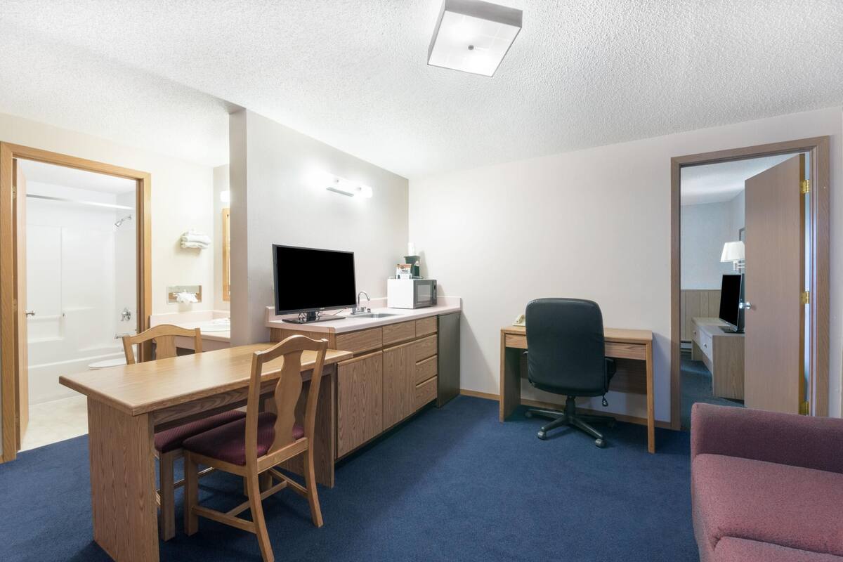 A hotel room with a wooden desk, a television, a microwave, a chair, and a bed.