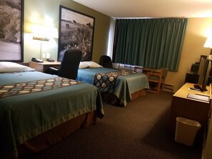 Habitación de hotel con dos camas, un escritorio, una silla, un cubo de basura y un cuadro grande en la pared.