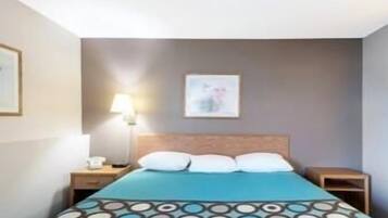 A hotel room with a bed, a nightstand, a lamp, and a framed picture on the wall.