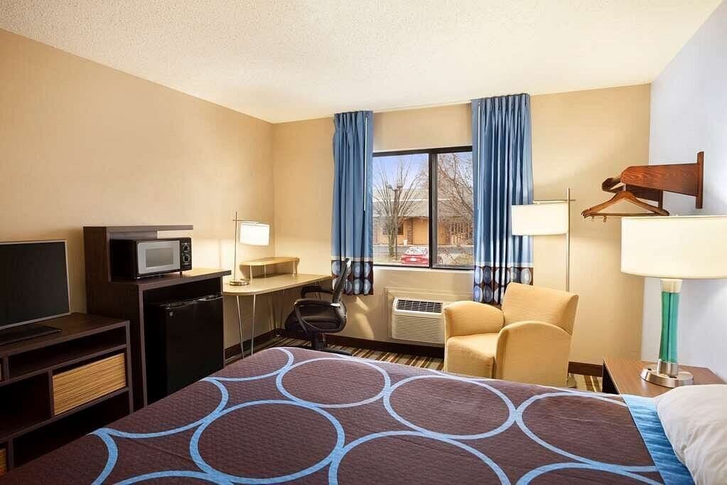A hotel room with a bed, desk, chair, TV, and a view of the outside.