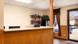 A reception area with a wooden reception desk, a plant, and a shelf with snacks. - Americas Best Value Inn Pittsburg (Pittsburg)