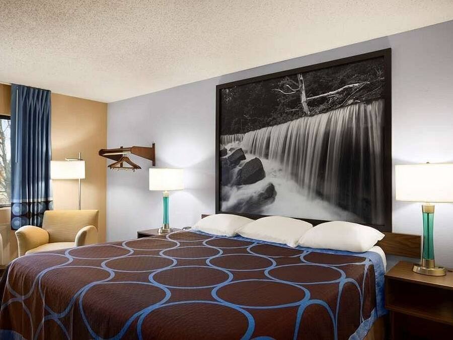 A hotel room with a large bed, two bedside tables, a chair, a window with curtains, and a large wall-mounted picture of a waterfall.
