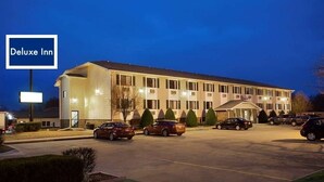 A hotel with a sign reading "Deluxe Inn," featuring a parking lot with several cars, a building with multiple windows, and a well-lit entrance. - Americas Best Value Inn Pittsburg (Pittsburg)