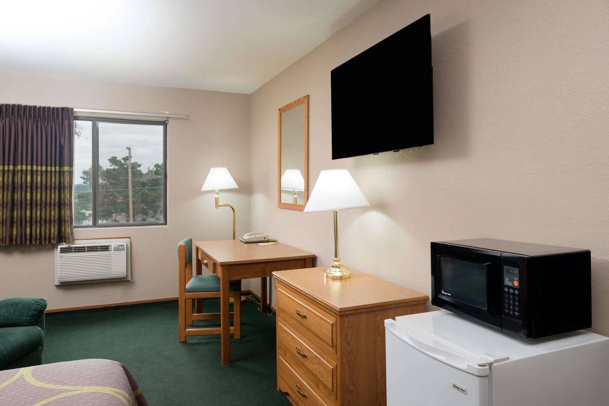 Une chambre d’hôtel équipée d’un bureau, de deux lampes, d’un téléviseur à écran plat, d’un four à micro-ondes, d’un réfrigérateur, d’une chaise, d’un lit et d’un climatiseur.