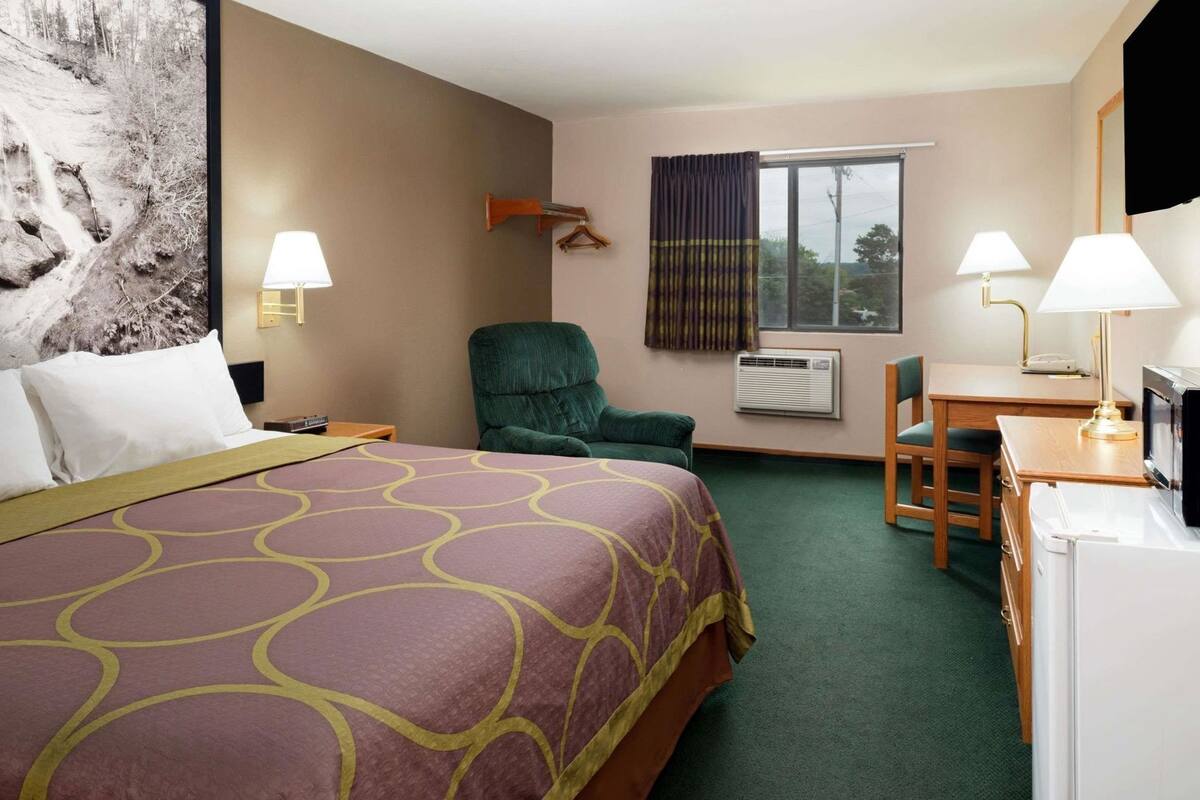 Une chambre d’hôtel équipée d’un lit, d’un bureau, d’une chaise, d’une télévision et d’une fenêtre avec des rideaux.