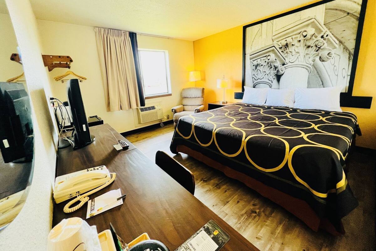 A hotel room with a bed, desk, chair, and a large artwork on the wall.