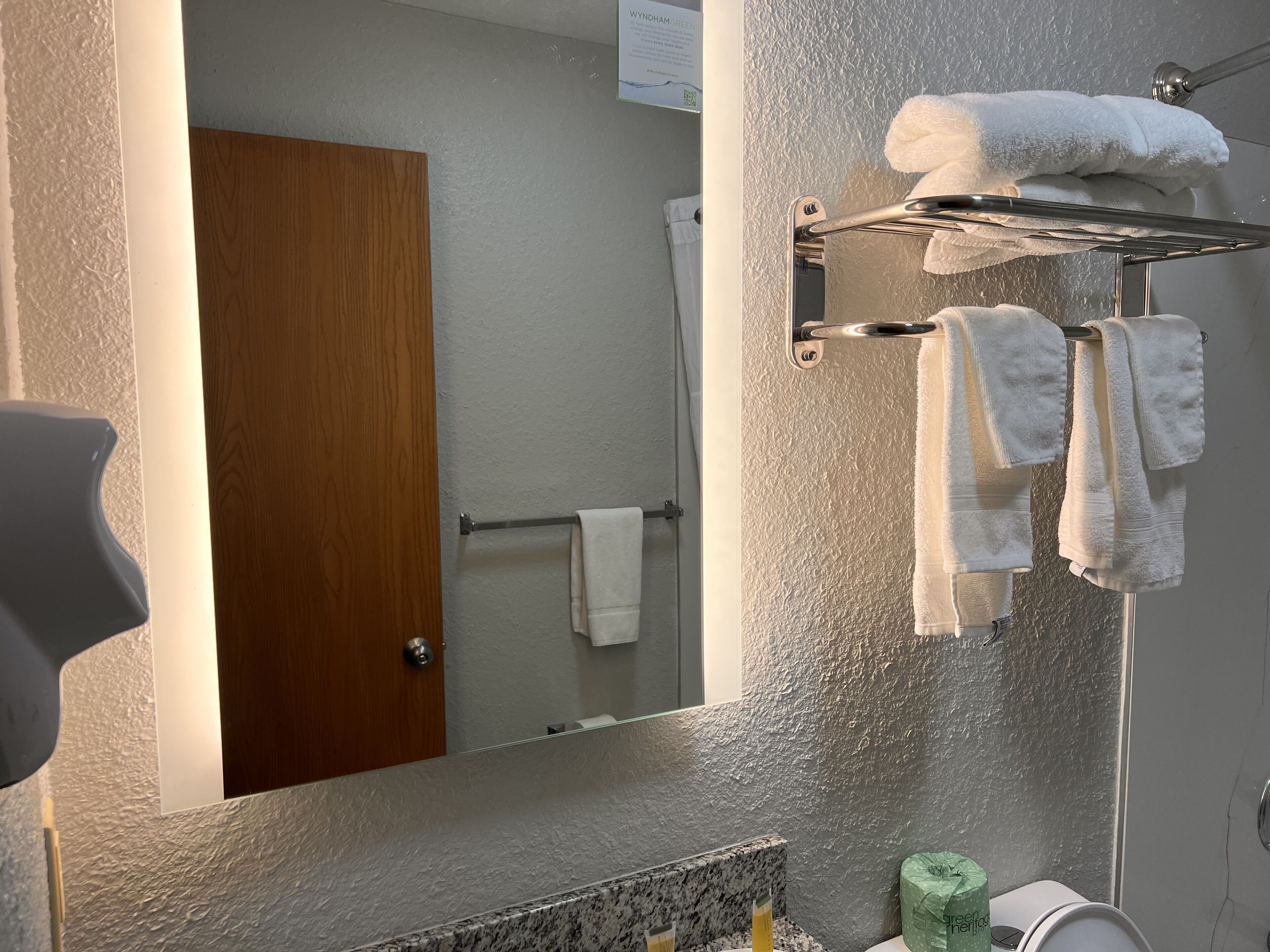 Une salle de bain dotée d’un grand miroir, d’un porte-serviettes avec plusieurs serviettes, d’une porte en bois et d’un comptoir en marbre.