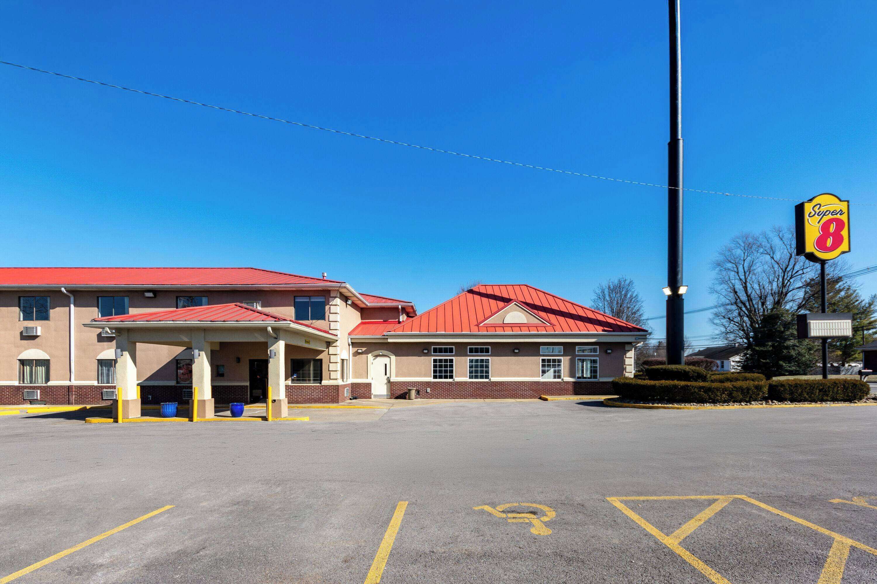 A Super 8 motel with a red roof, a covered parking area, and a clear blue sky.