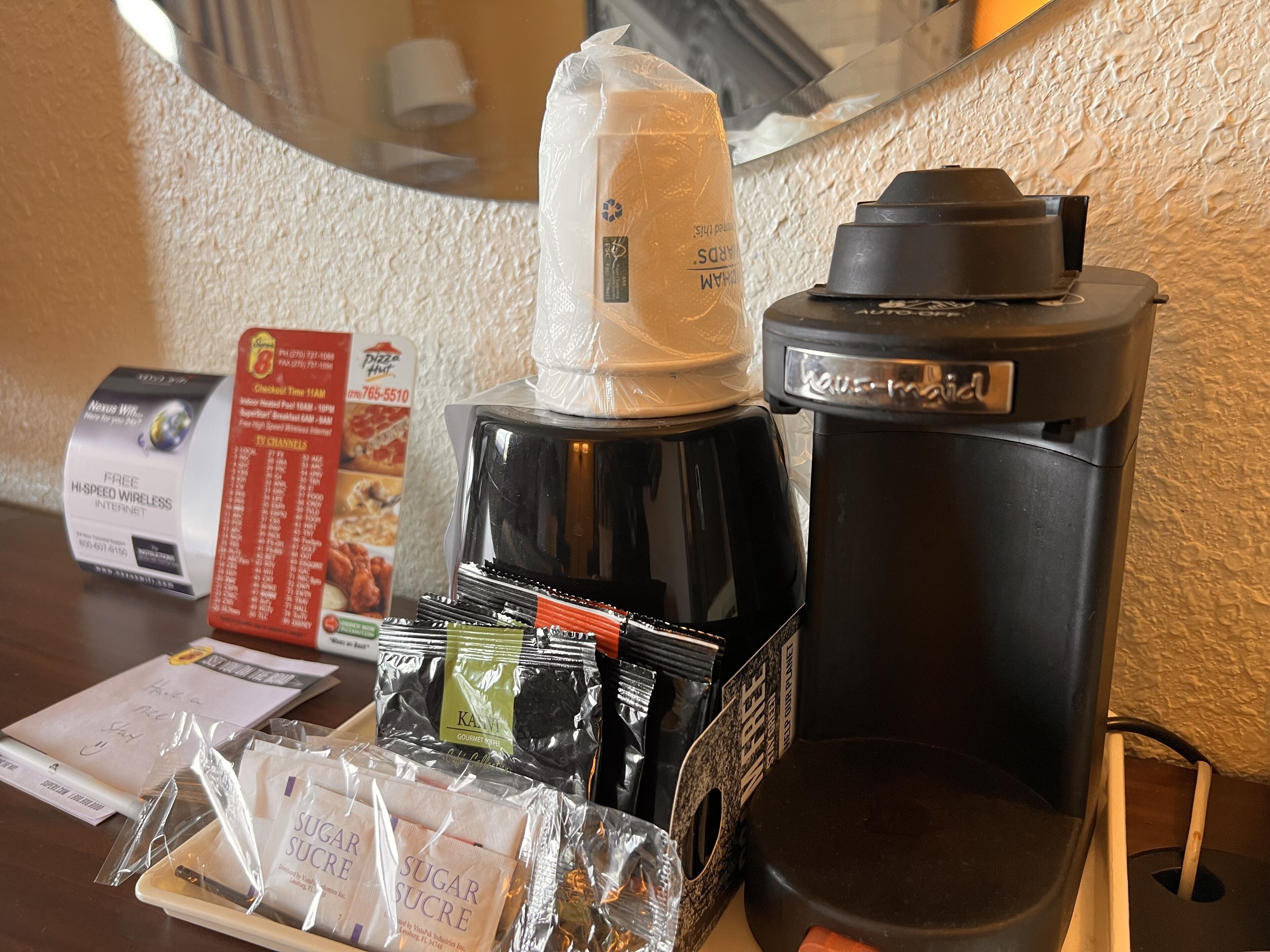 Une machine à café, une bouilloire, un menu et un panneau indiquant la présence d’une connexion Wi-Fi sur une table d’hôtel.