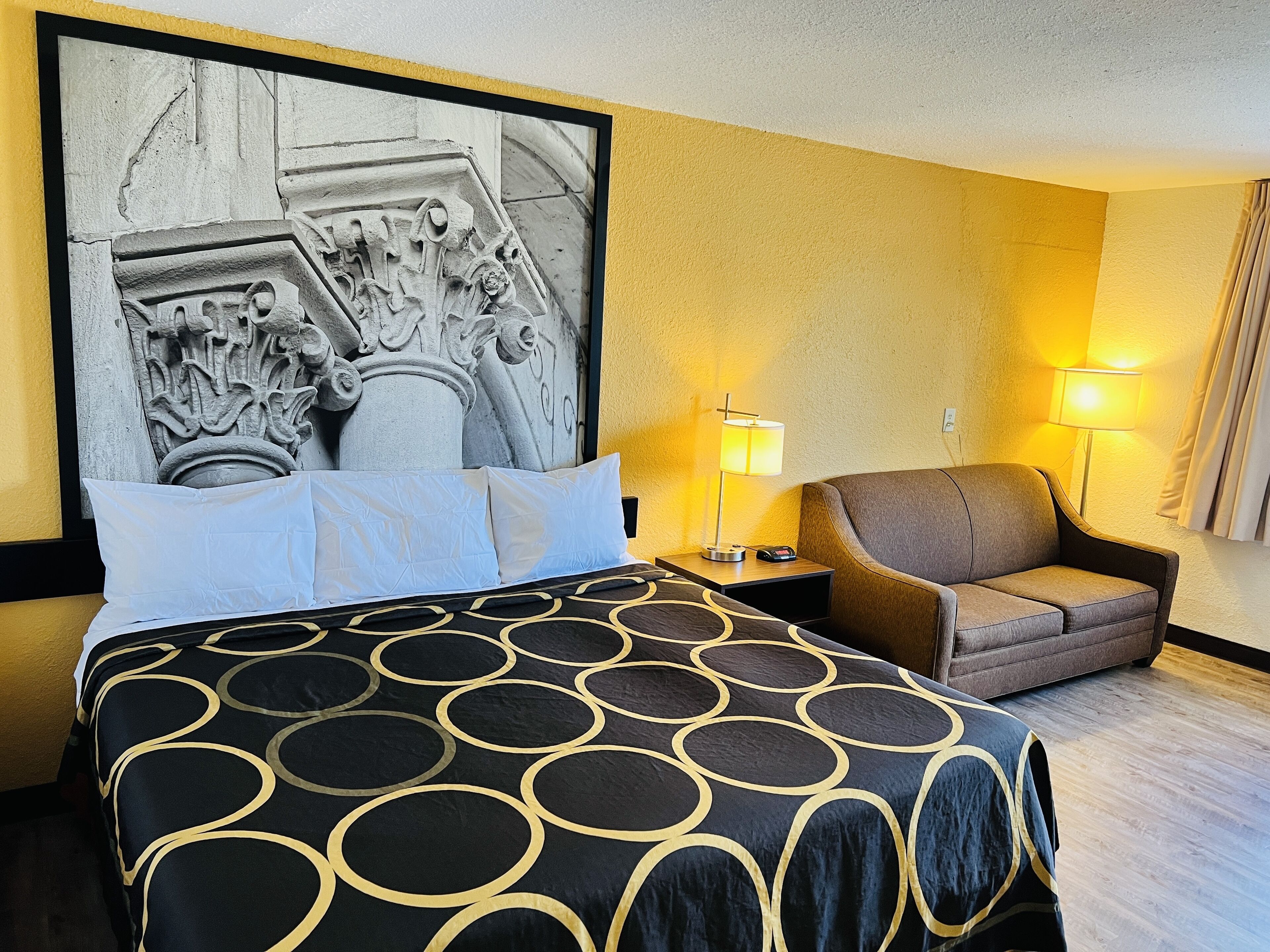 Une chambre d’hôtel avec un grand lit, deux tables de chevet, une chaise et une œuvre d’art accrochée au mur.