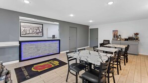 Un hall d’hôtel comprenant un comptoir d’accueil, un espace repas avec des tables et des chaises, une cuisine et un espace de réception agrémenté d’une photographie encadrée.