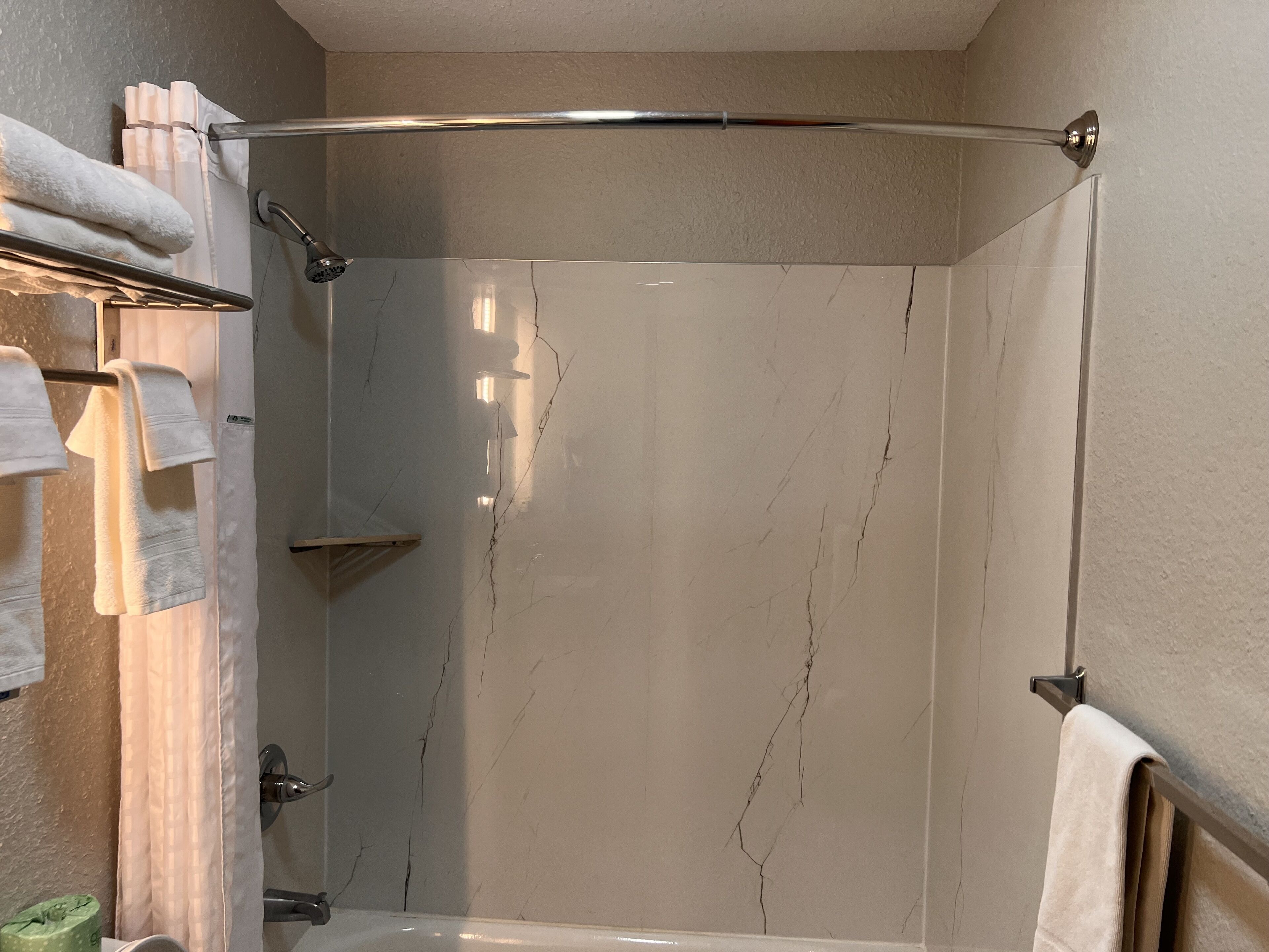 Un baño moderno con cabina de ducha de vidrio, un perchero con varias toallas y ducha visible.