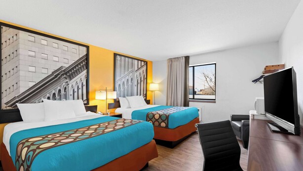 Une chambre d’hôtel avec deux lits, un bureau, une télévision et une grande fenêtre donnant sur un immeuble.