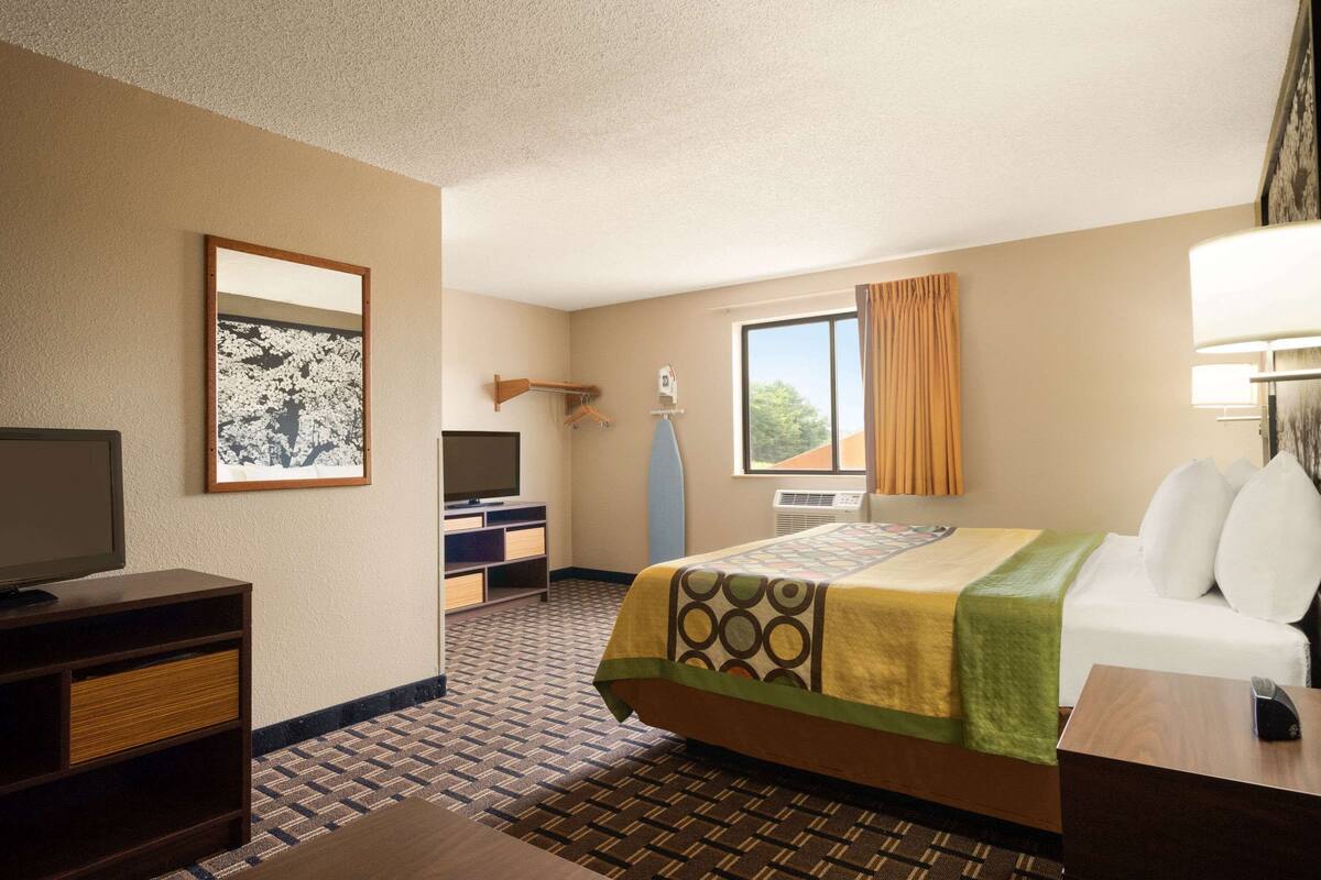 Ein Hotelzimmer mit Bett, Fernseher, Schreibtisch, Stuhl und einem Fenster mit Vorhängen.