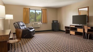 Une chambre d’hôtel avec un fauteuil en cuir, un bureau, une télévision et une grande fenêtre avec des rideaux.