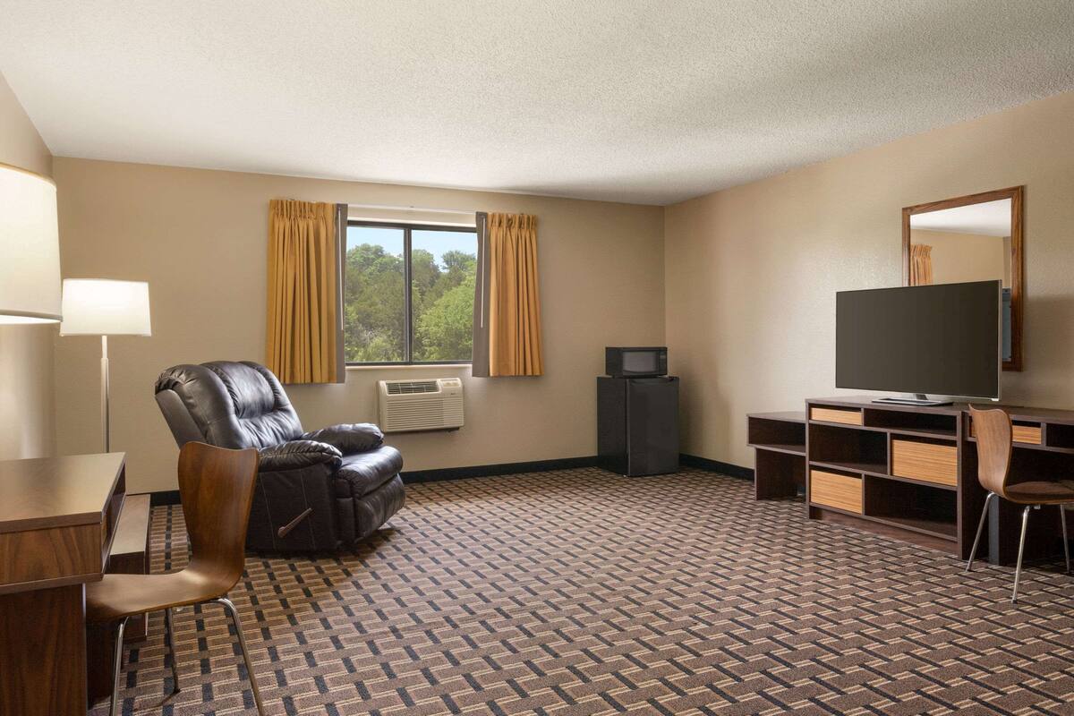 Ein Hotelzimmer mit Ledersessel, Schreibtisch, Fernseher und großem Fenster mit Vorhängen.