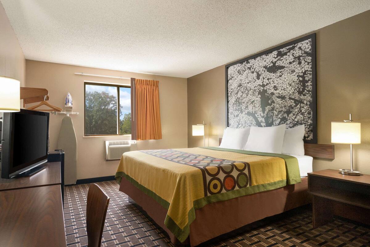 Ein Hotelzimmer mit einem Bett, einem Fernseher, einem Schreibtisch und einem großen Fenster mit Vorhängen.