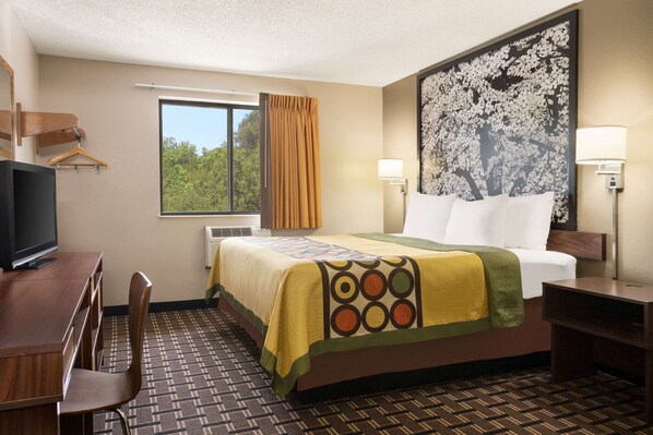 Habitación de hotel con cama, escritorio con silla, televisión, ventana con cortinas y una obra de arte colgada en la pared.