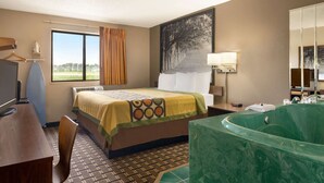Une chambre d’hôtel avec un lit, un bureau, une chaise, une grande fenêtre, un tableau, une baignoire verte et un miroir.
