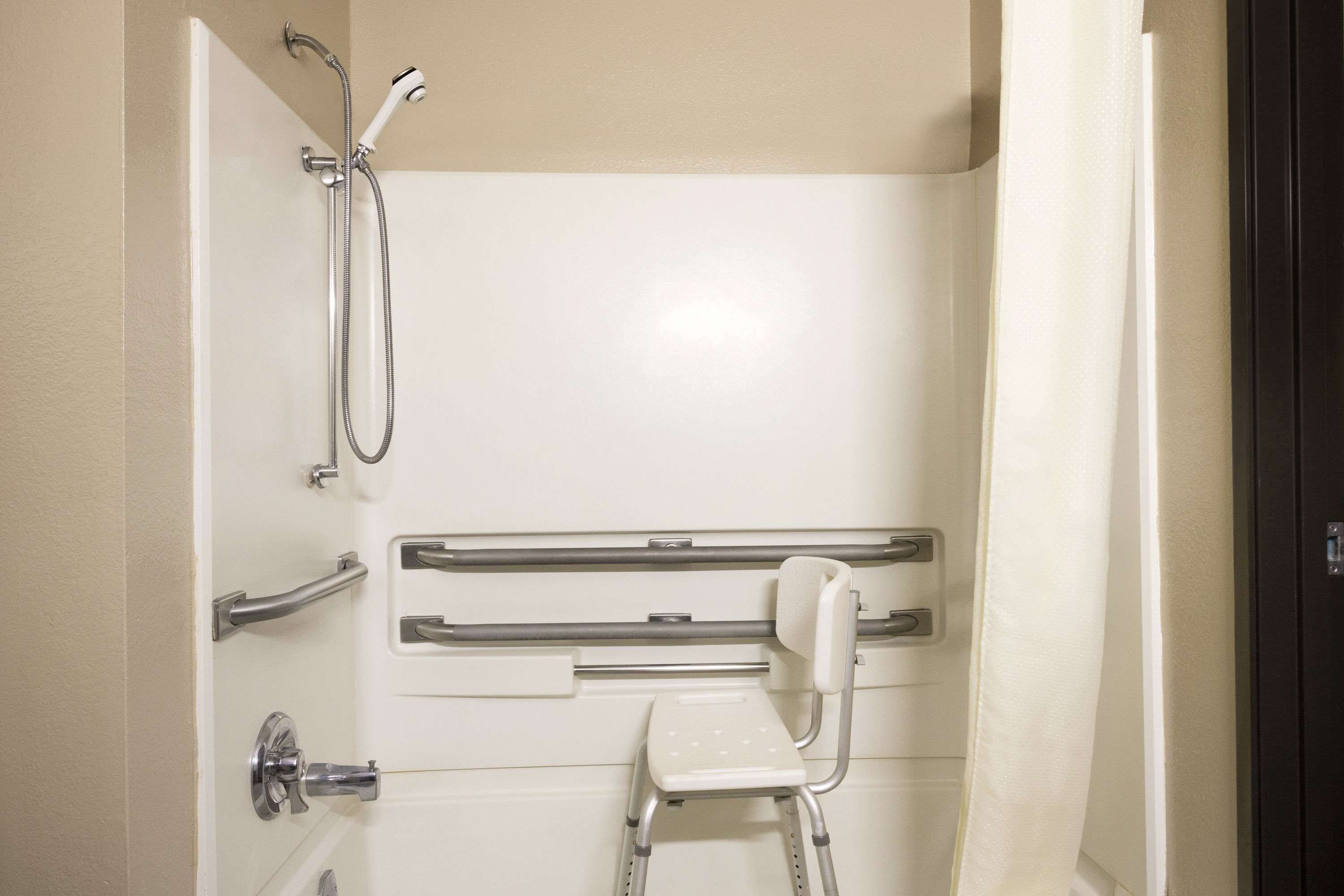 Un baño con ducha, barras de apoyo y asiento accesible para sillas de ruedas.