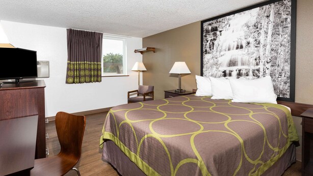 Une chambre d’hôtel avec un grand lit, un bureau avec une télévision, deux lampes, une chaise et un grand tableau encadré au mur.
