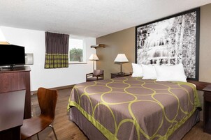 A hotel room with a large bed, a desk with a television, two lamps, a chair, and a large framed picture on the wall.