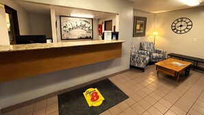 Un espace d’accueil avec un comptoir en bois, une affiche encadrée, des chaises à motifs, une horloge et une table basse en bois.