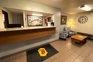 A reception area with a wooden counter, a framed poster, patterned chairs, a clock, and a wooden coffee table.