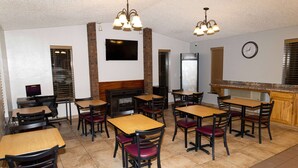 Un restaurant avec des tables et des chaises en bois, une cheminée en briques et une horloge au mur.