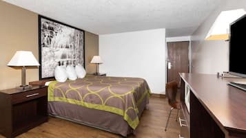 A hotel room with a large bed, two bedside lamps, a desk with a TV, and a large framed picture on the wall.