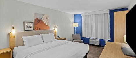A hotel room with a bed, bedside tables, a desk, a chair, a lamp, a painting, and a window with curtains.