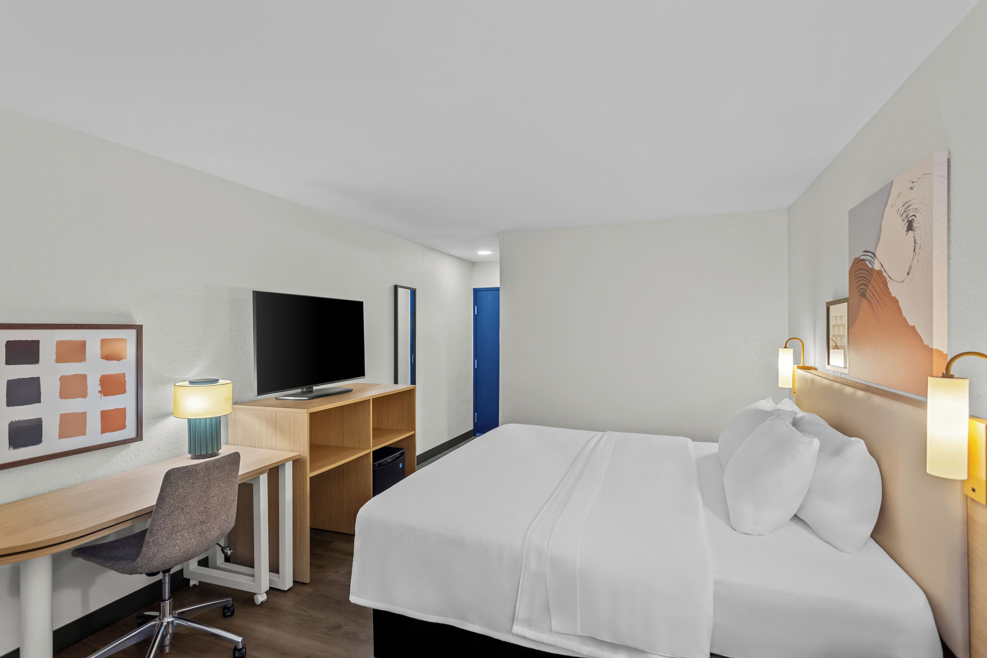 Une chambre d’hôtel équipée d’un lit, d’un bureau, d’une chaise, d’une télévision et d’œuvres d’art accrochées au mur.