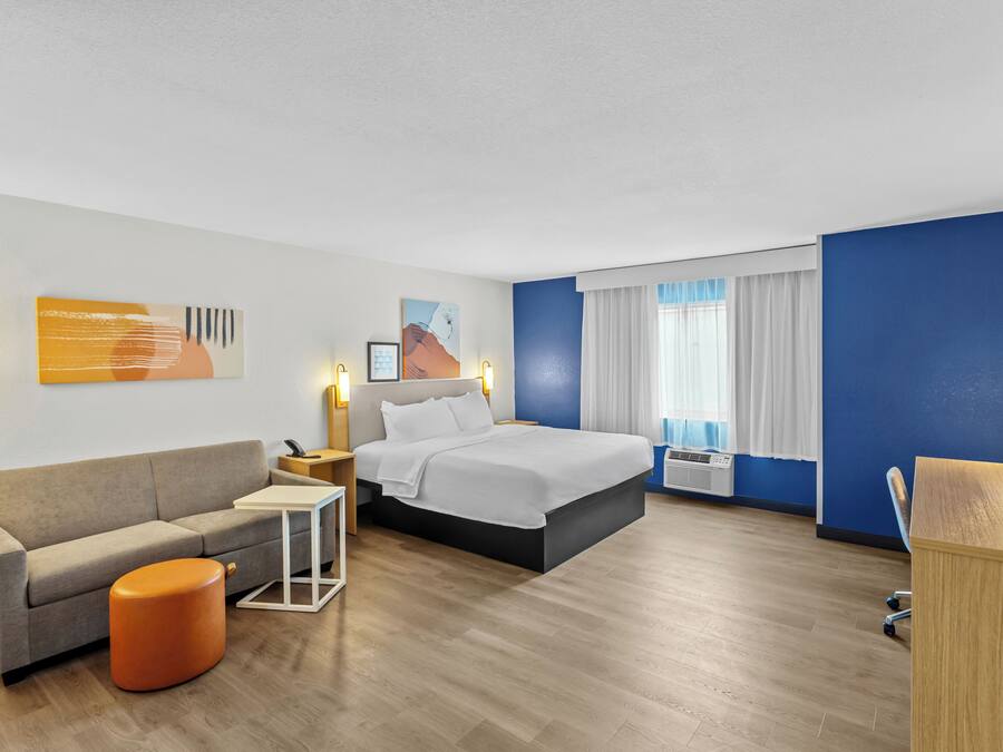 Quarto de hotel com cama, sofá, mesa pequena e uma cadeira.