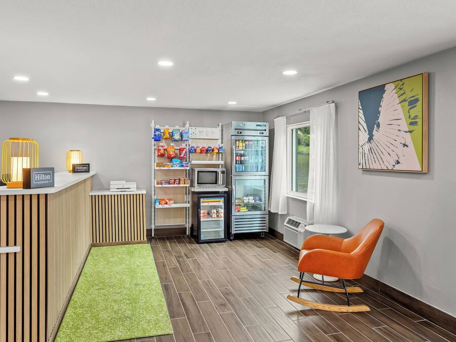 A hotel lobby with a reception desk, a seating area with a rocking chair, a vending machine, and a refrigerator.