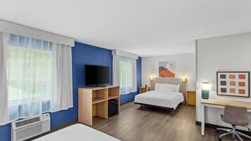 A hotel room with a bed, a desk, a chair, a television, and a painting on the wall.