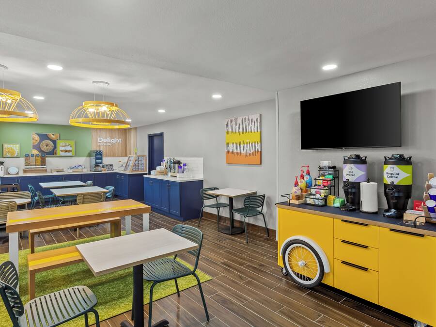 A modern kitchen with a coffee station, a flat-screen TV, and a dining area with tables and chairs.