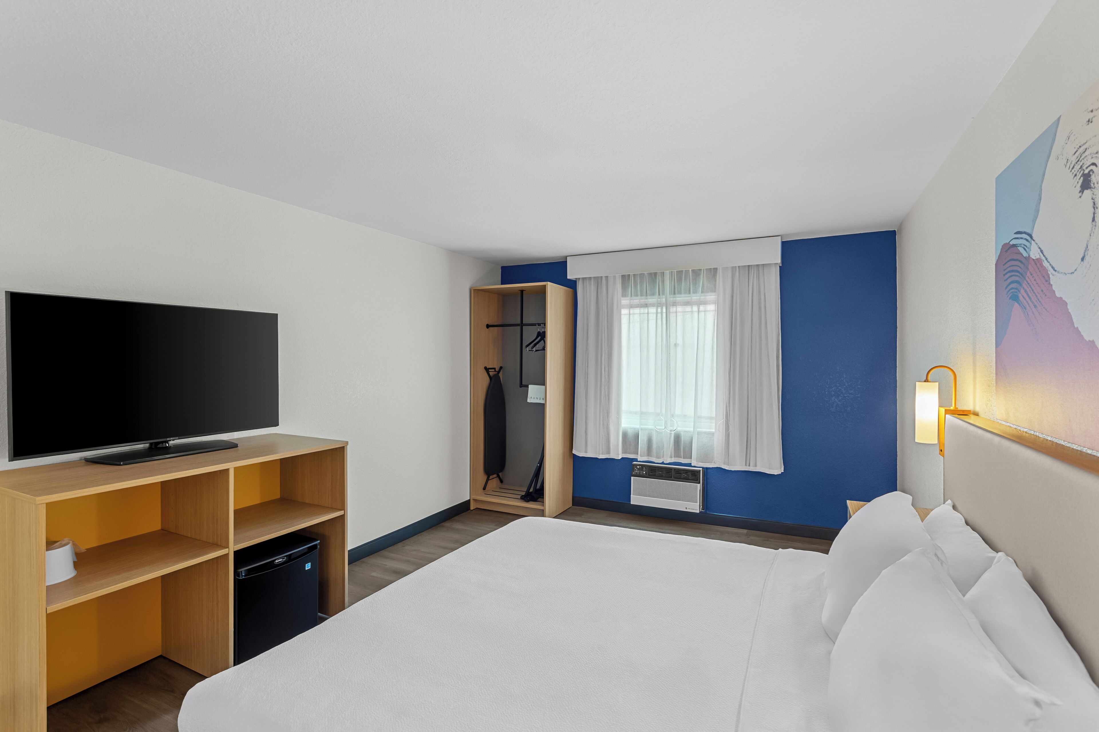 A hotel room with a bed, a TV, a wardrobe, and a window with curtains.